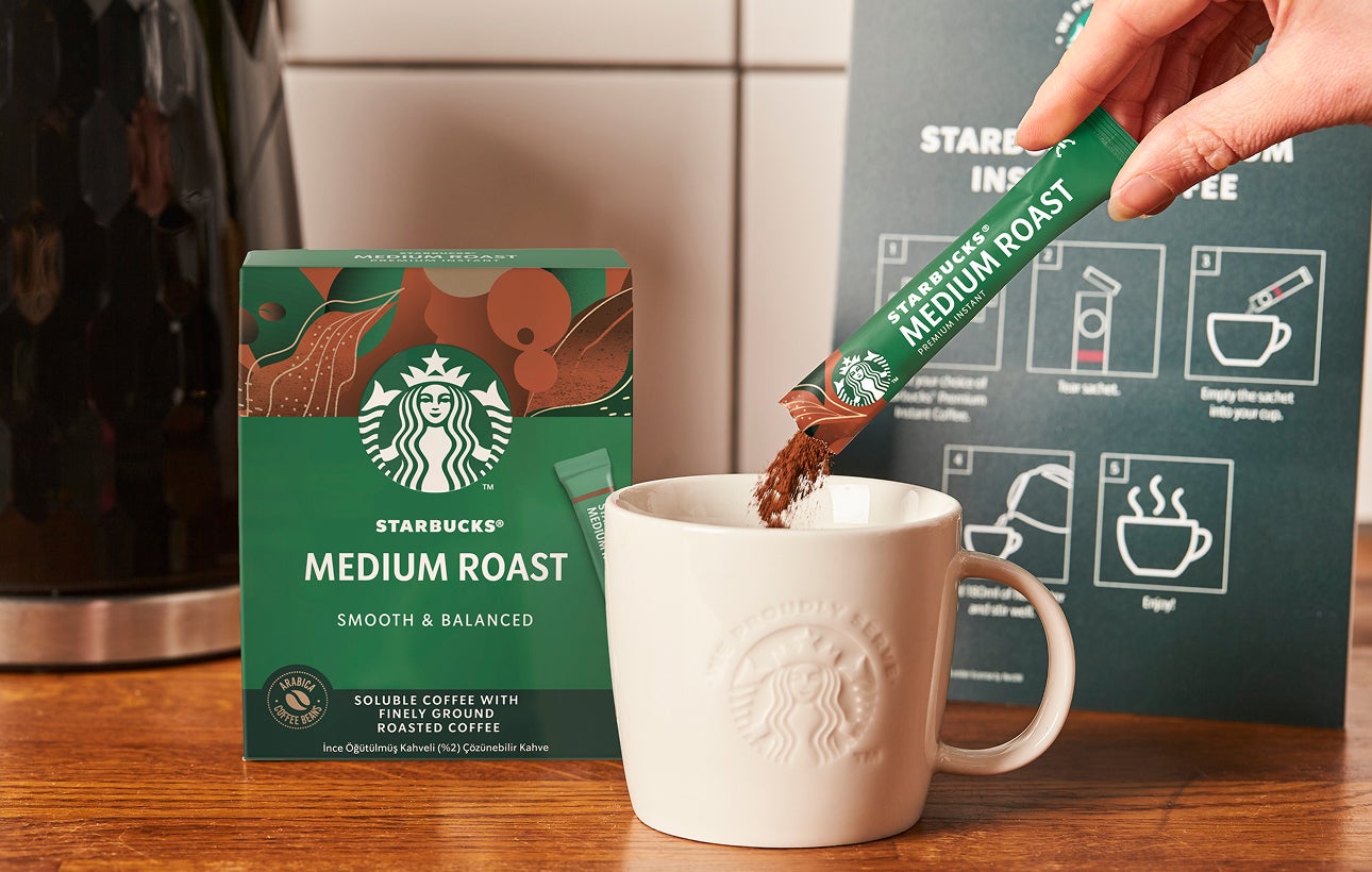 Un pliculeț de cafea Starbucks Premium Instant Medium Roast turnat într-o cană de ceramică We Proudly Serve Starbucks