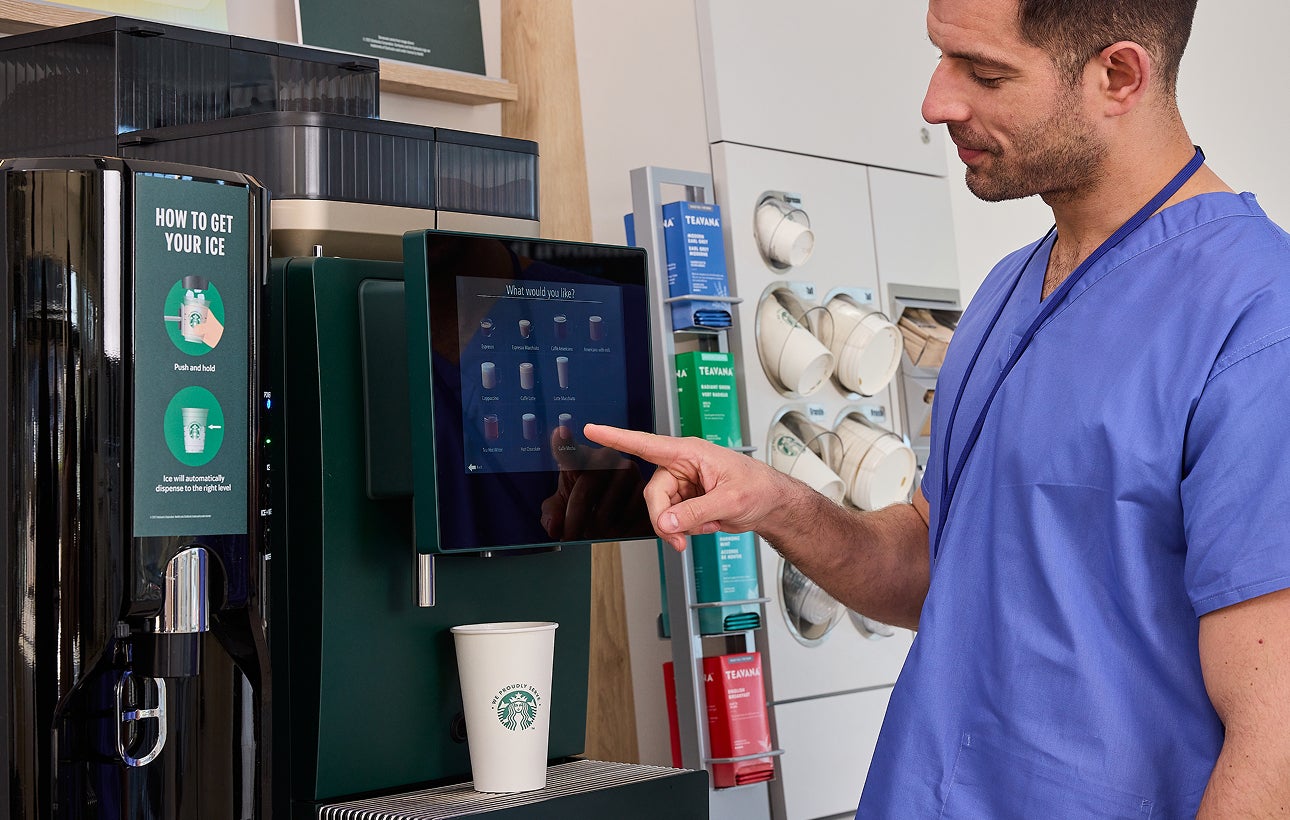 Cadru medical care selectează o băutură la aparatul de cafea cu autoservire We Proudly Serve Starbucks. 
