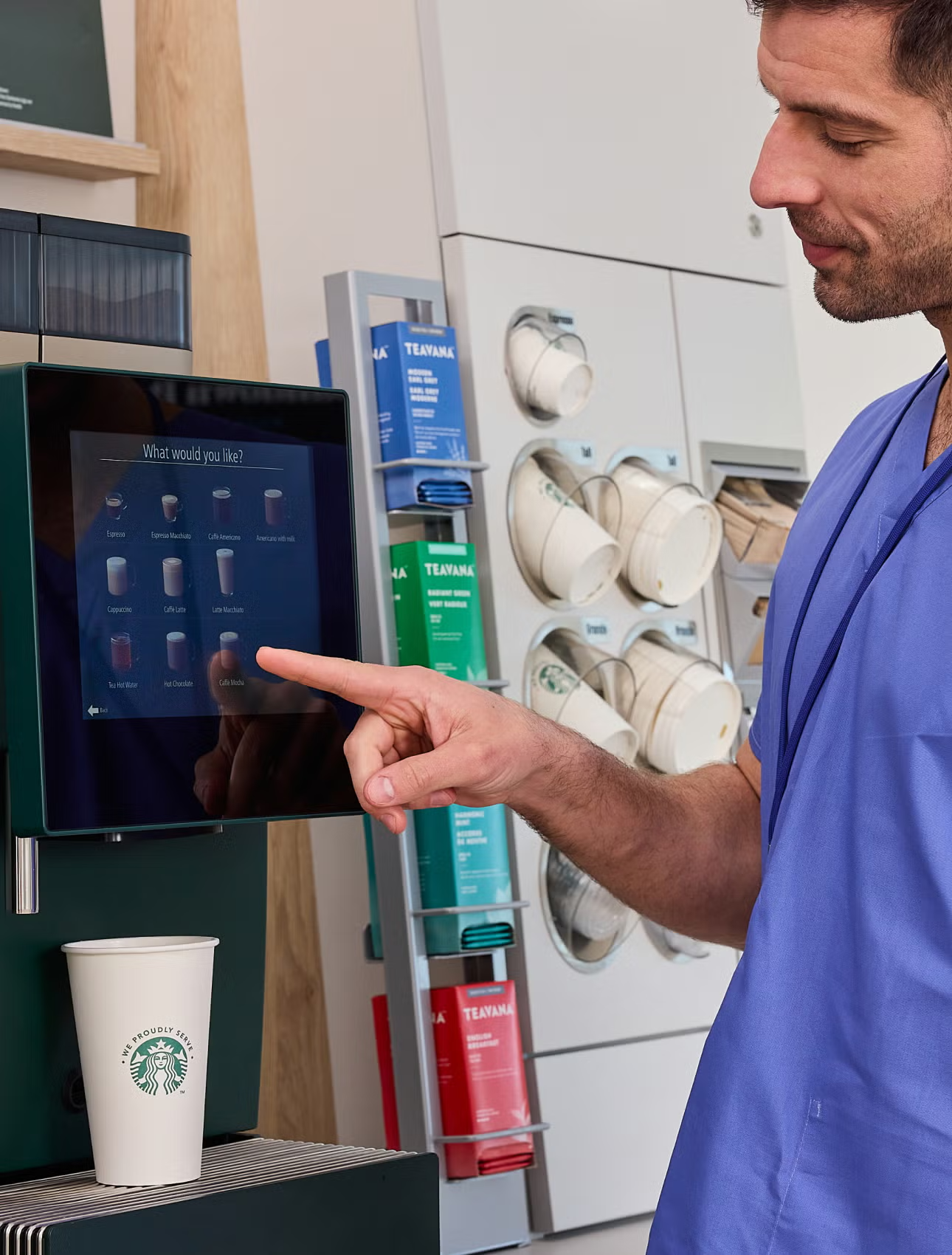 Cadru medical care selectează o băutură la aparatul de cafea cu autoservire We Proudly Serve Starbucks. 
