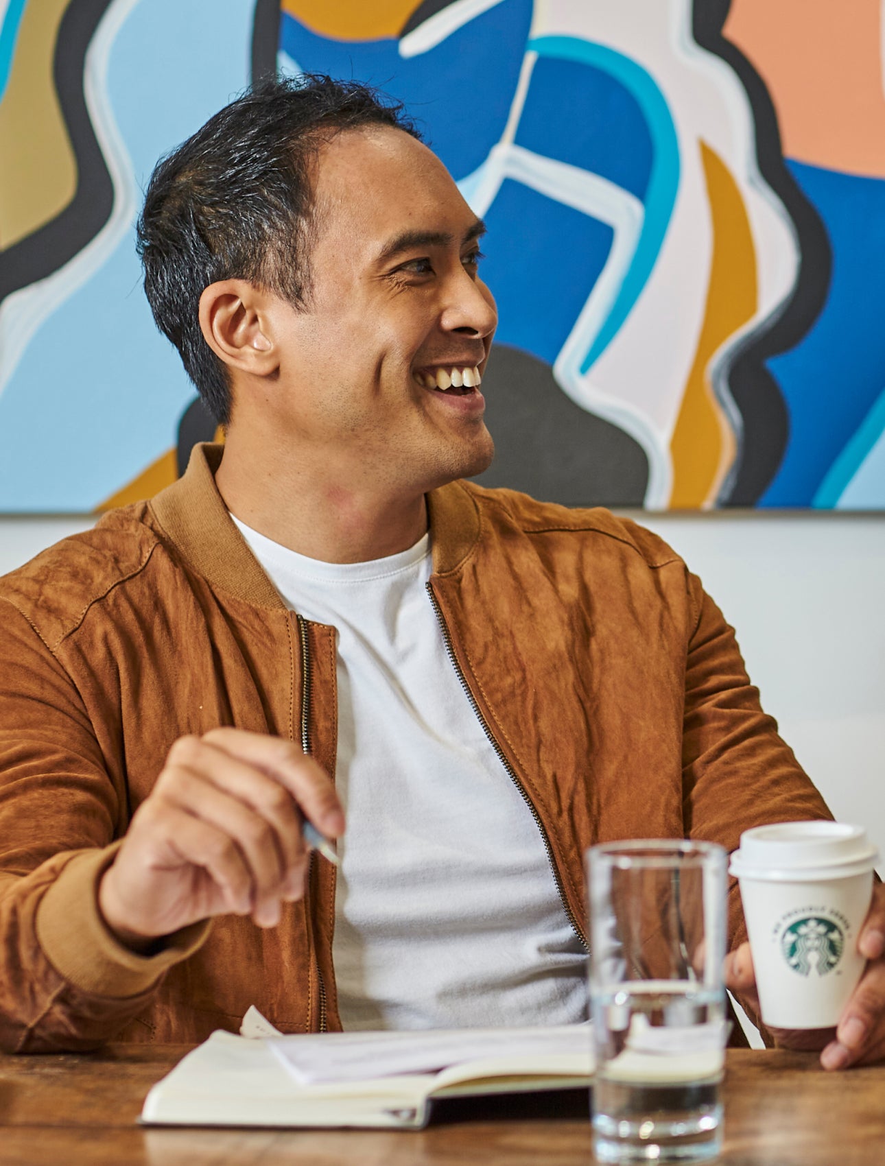 Bărbați așezați la o masă ținând în mână cafeaua We Proudly Serve Starbucks