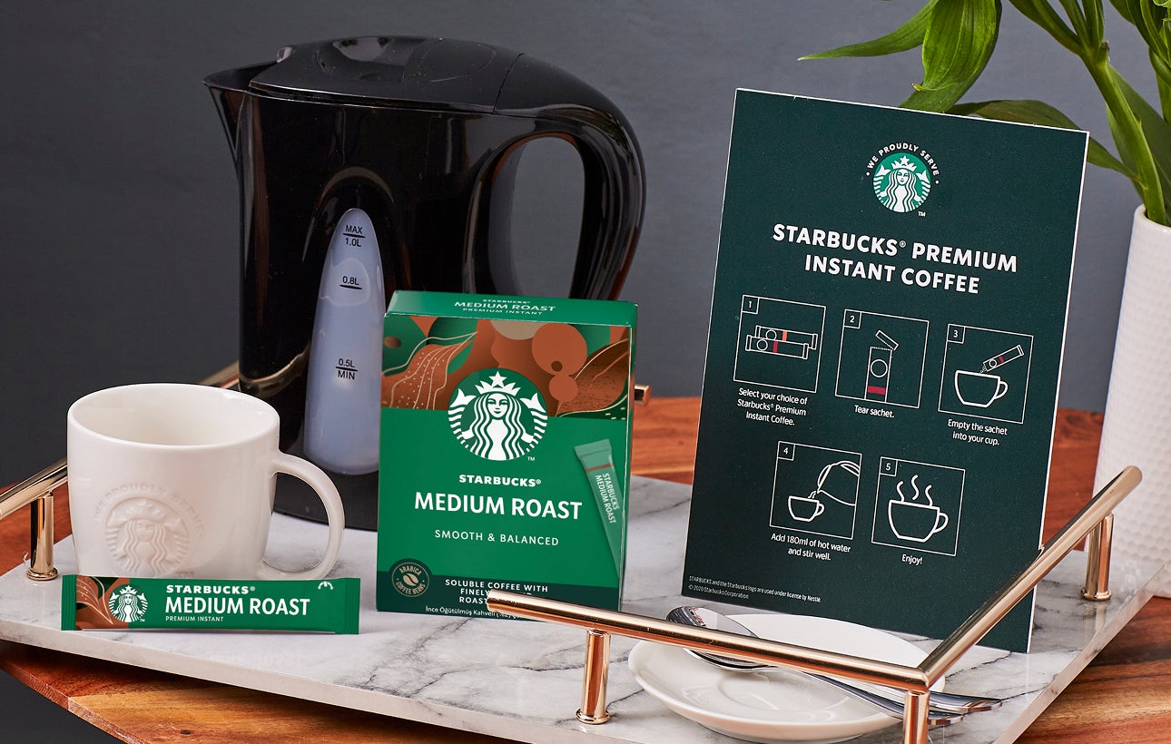 Blat de masă cu o cană We Proudly Serve Starbucks, cafea Starbucks Premium Instant și instrucțiuni de preparare