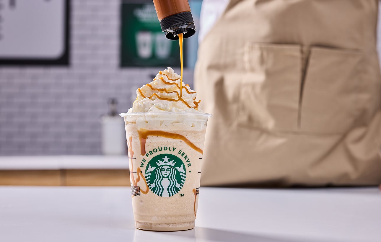 O băutură Starbucks amestecată cu frișcă și un barista care adaugă un strop de caramel 