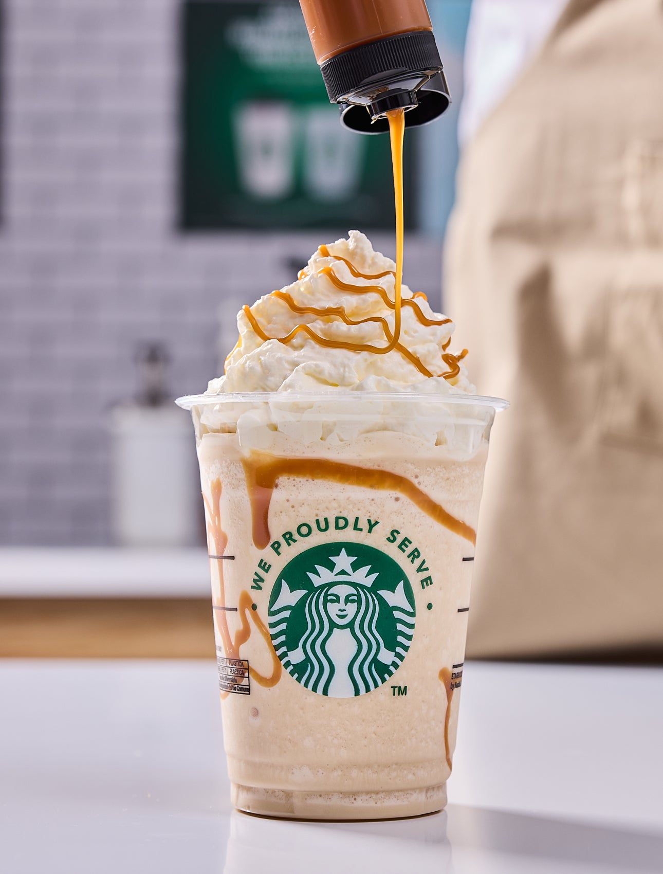 O băutură Starbucks amestecată cu frișcă și un barista care adaugă un strop de caramel 