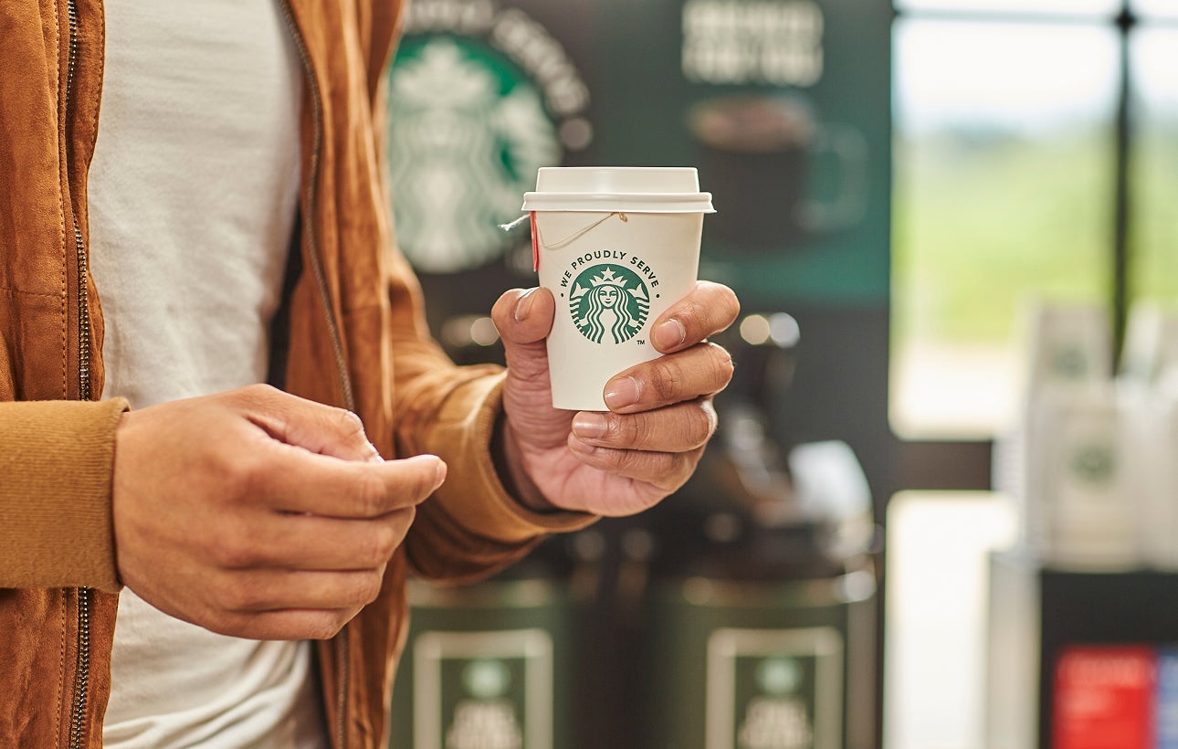 O persoană ținând o ceașcă de ceai într-o ceașcă la pachet We Proudly Serve Starbucks