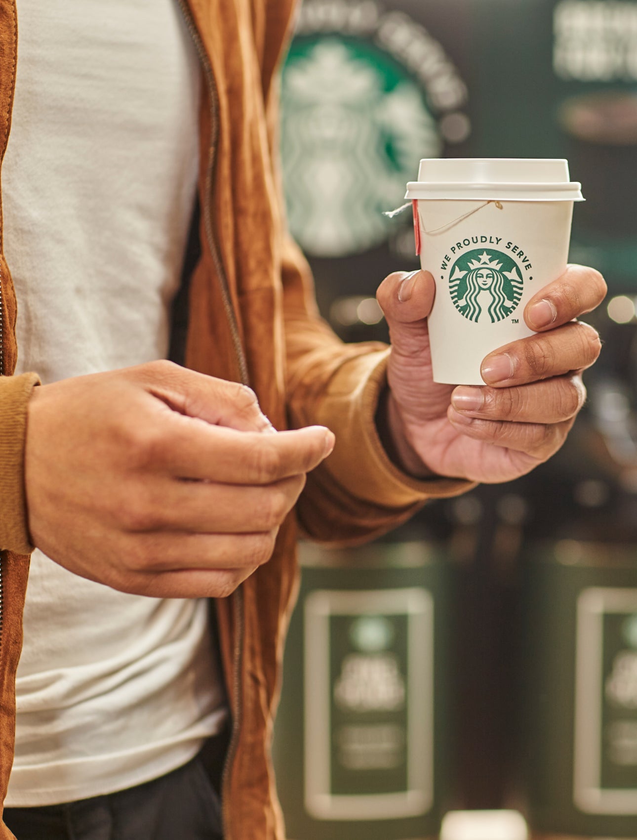 O persoană ținând o ceașcă de ceai într-o ceașcă la pachet We Proudly Serve Starbucks