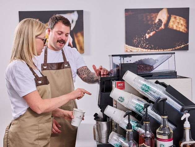 Doi barista purtând șorțuri, operând un aparat de cafea aprobat de Starbucks