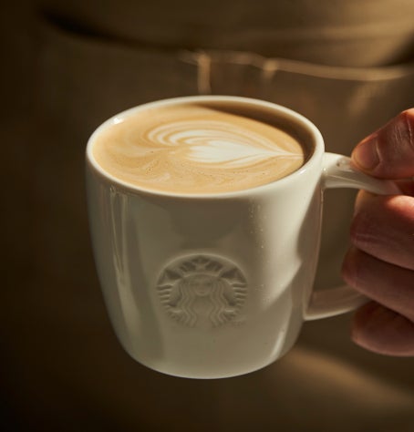 Turnarea laptelui într-o cană Starbucks de ceramică pentru a crea artă latte