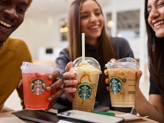 Un grup de prieteni zâmbitori țin în mână trei băuturi cu gheață de la Starbucks