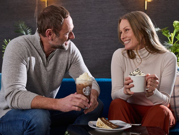 Un bărbat și o femeie stând împreună, savurând băuturi calde și reci de la Starbucks