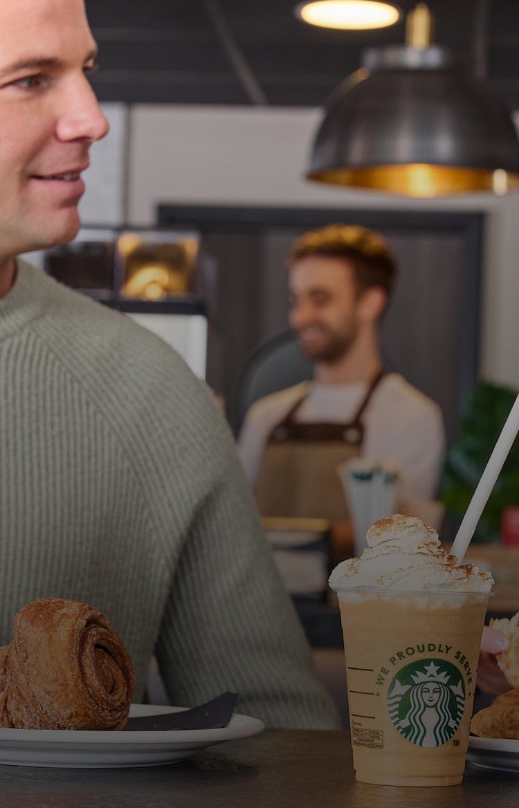 Un bărbat și o femeie își zâmbesc unul altuia într-o cafenea în timp ce savurează o cafea Starbucks