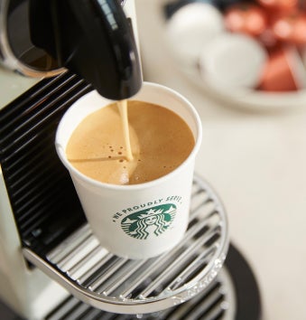 O ceașcă We Proudly Serve Starbucks umplută cu cafea proaspăt preparată la un aparat de espresso cu doză porționată