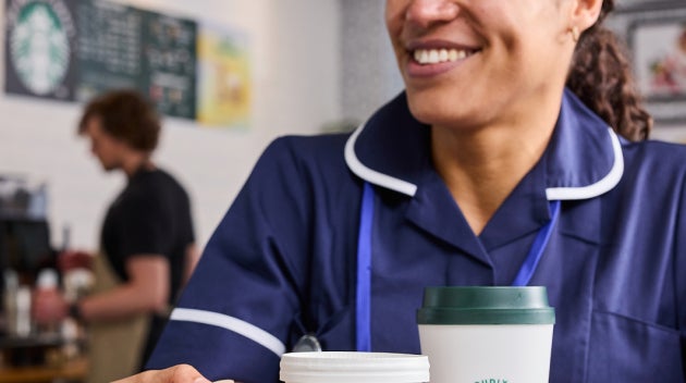 Profesioniști din domeniul sănătății stând împreună într-o cafenea a unui spital, ținând în mână băuturi We Proudly Serve Sta