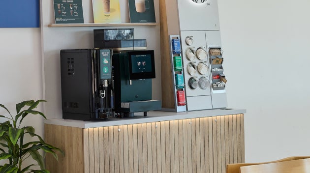 O stație compactă de cafea We Proudly Serve Starbucks în zona de ambulatoriu a unui spital, dotată cu un aparat de cafea cu a